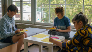 3 people sitting around table, writing